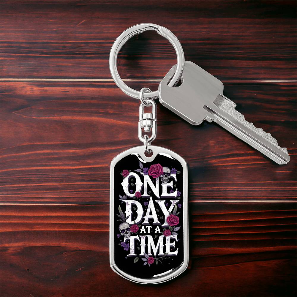 Silver dog tag keychain with “One Day At A Time” front and attached house key