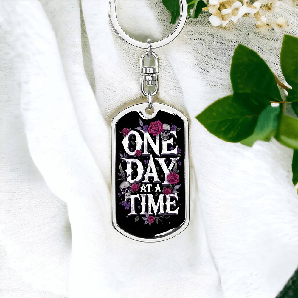 Silver dog tag keychain with “One Day At A Time” front design and floral skull detail