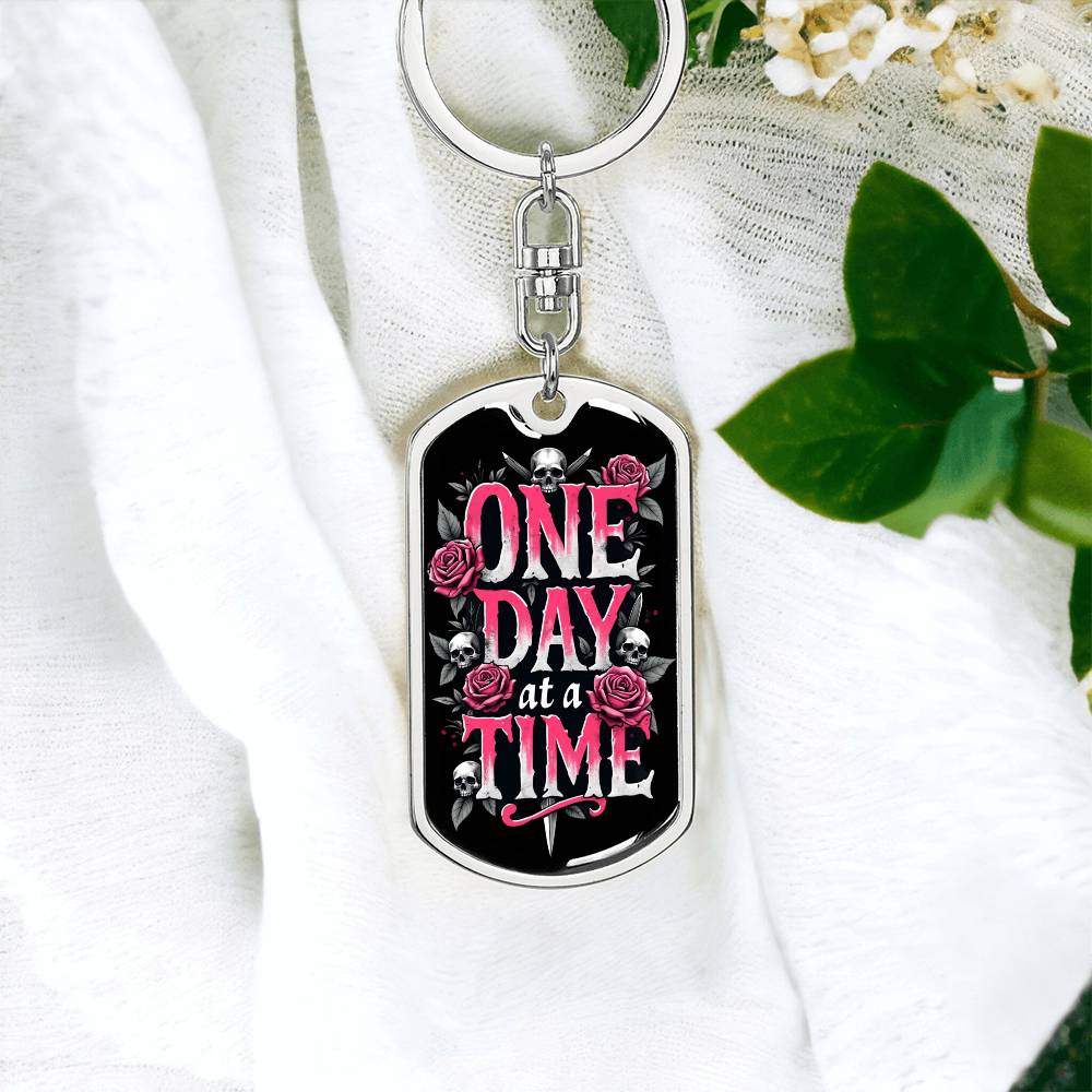 Silver dog tag keychain with black graphic and pink “One Day at a Time” text