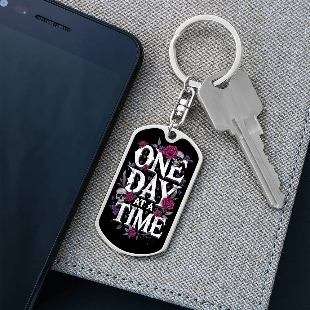 Silver dog tag keychain with black enamel face, floral skull design and engraved text