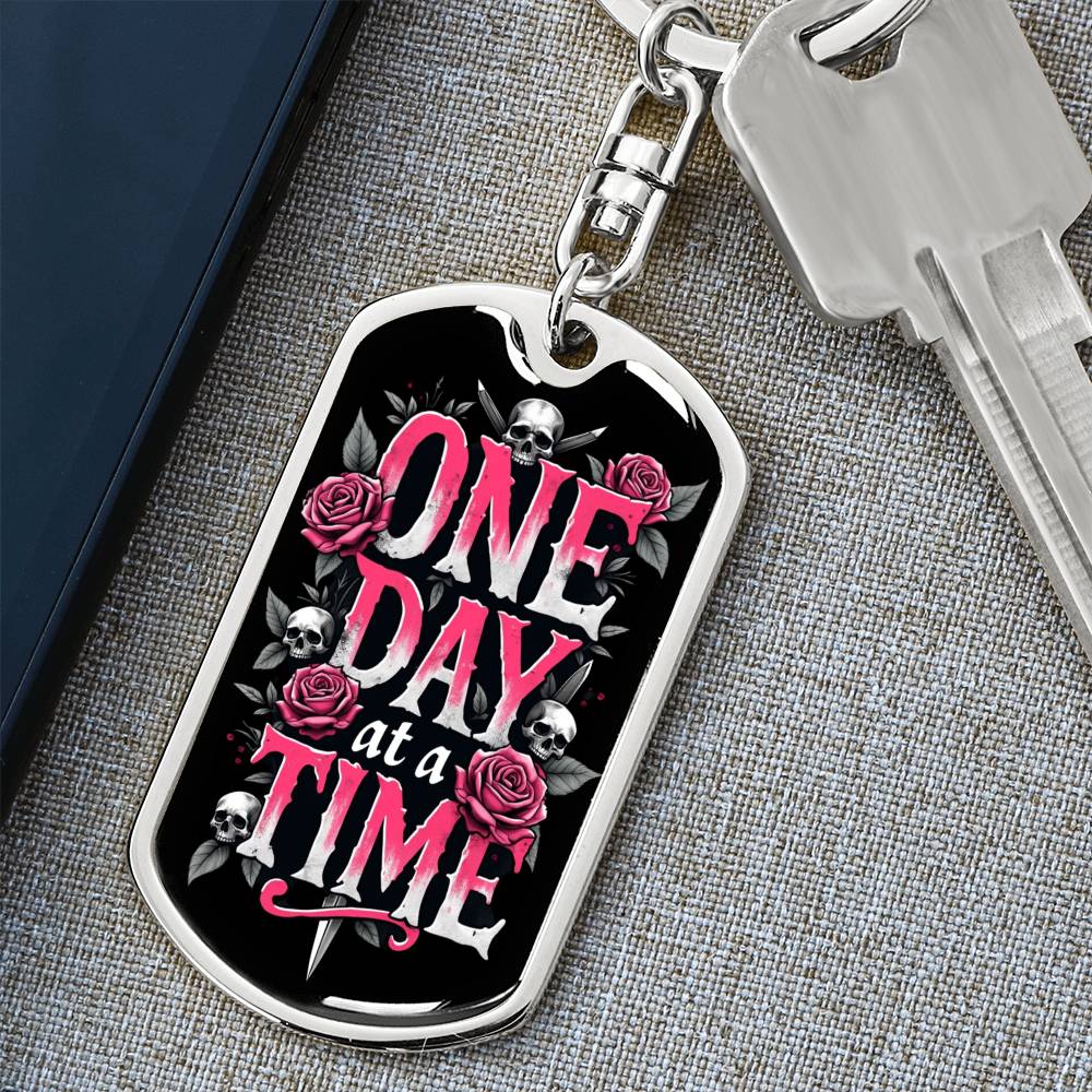 Silver dog tag keychain with black graphic and pink “One Day at a Time” text