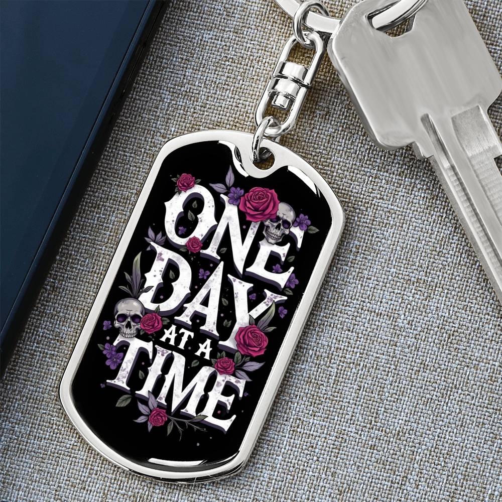Silver dog tag keychain with “One Day At A Time” design, roses, and skull accents