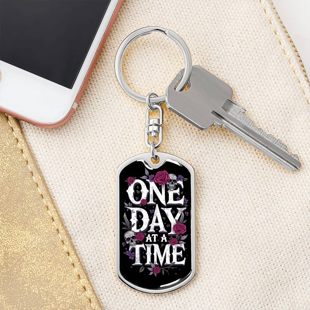 Silver dog tag keychain with “One Day At A Time” front and attached house key