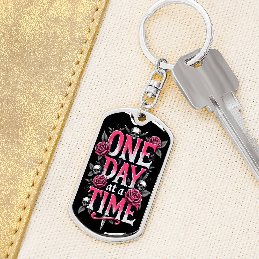 Gold dog tag keychain with black graphic and pink text on a small key