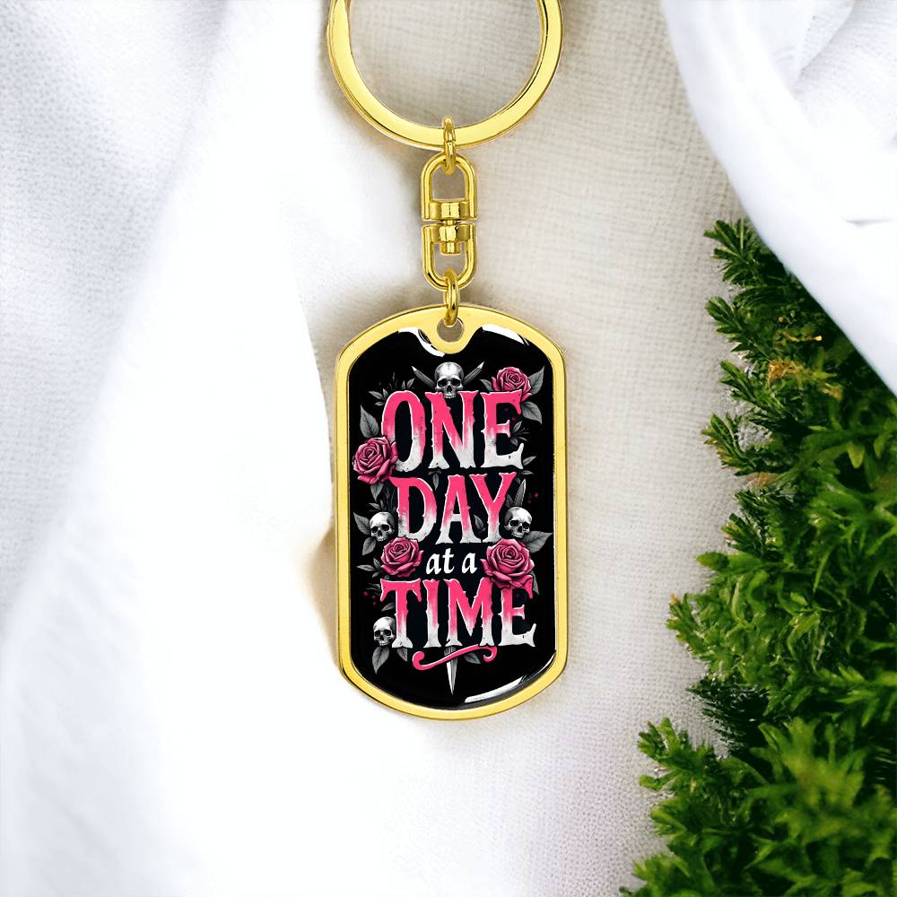 Gold dog tag keychain, black insert with One Day at a Time text, roses and skulls