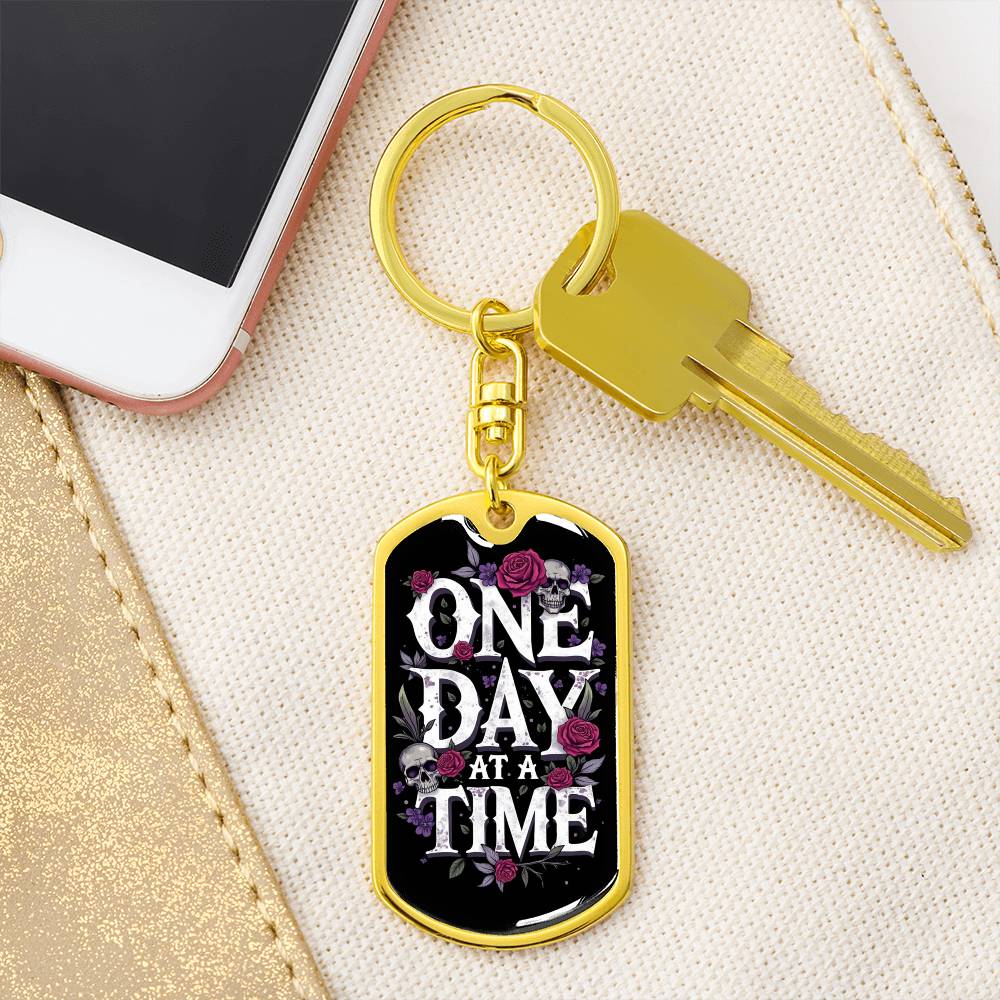 Gold dog tag keychain with “One Day At A Time” front and attached house key