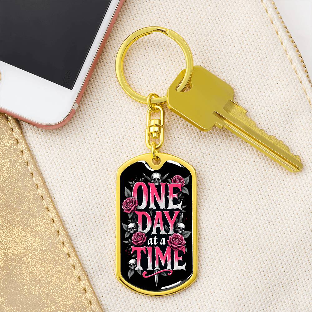 Gold dog tag keychain with black graphic and pink text on a keyring