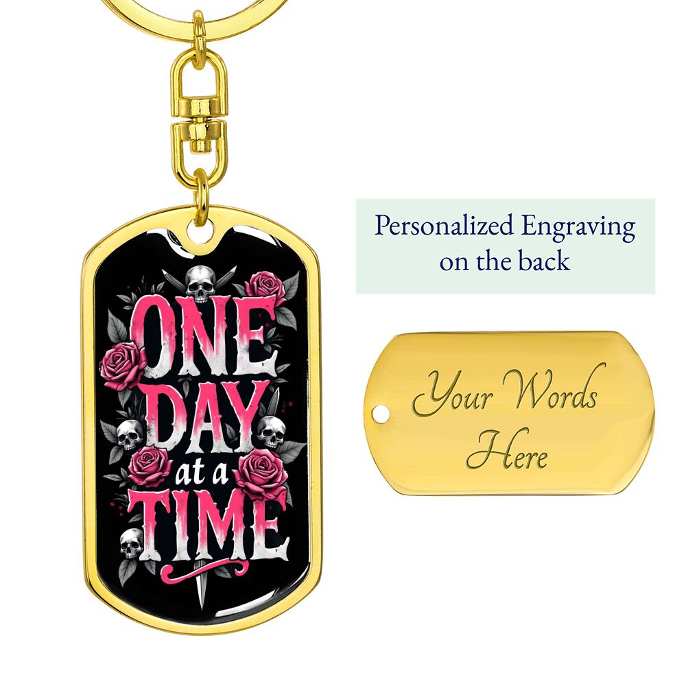 Gold dog tag keychain with black graphic and pink text, plus engraved back panel