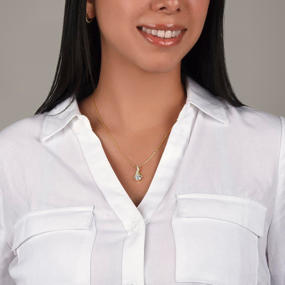 Gold-tone teardrop pendant necklace on a fine chain, worn with a white shirt