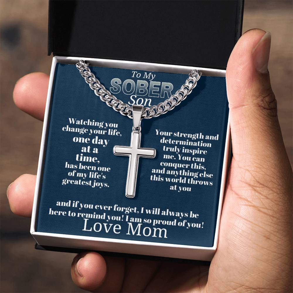 Silver-tone cross pendant necklace on blue card inside gift box held in hand