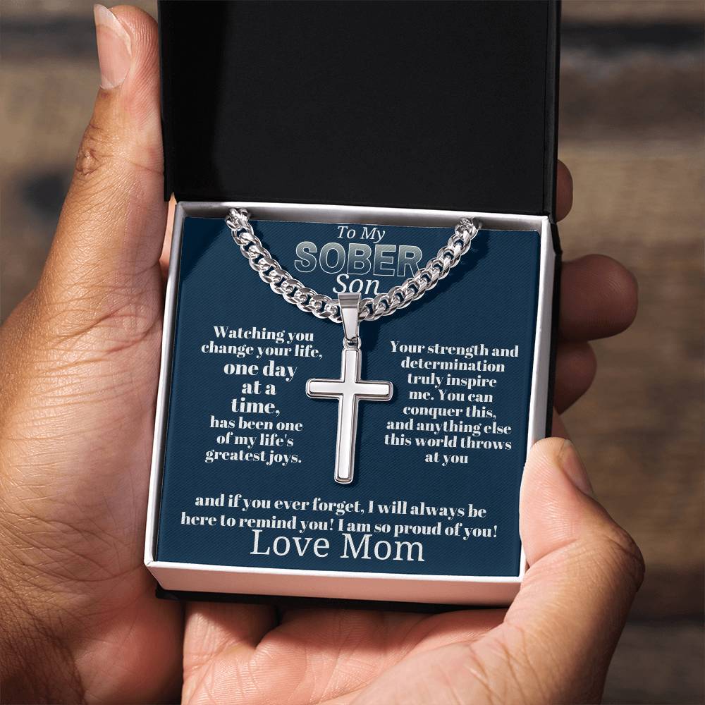 Silver-tone cross pendant necklace in open gift box held above hands