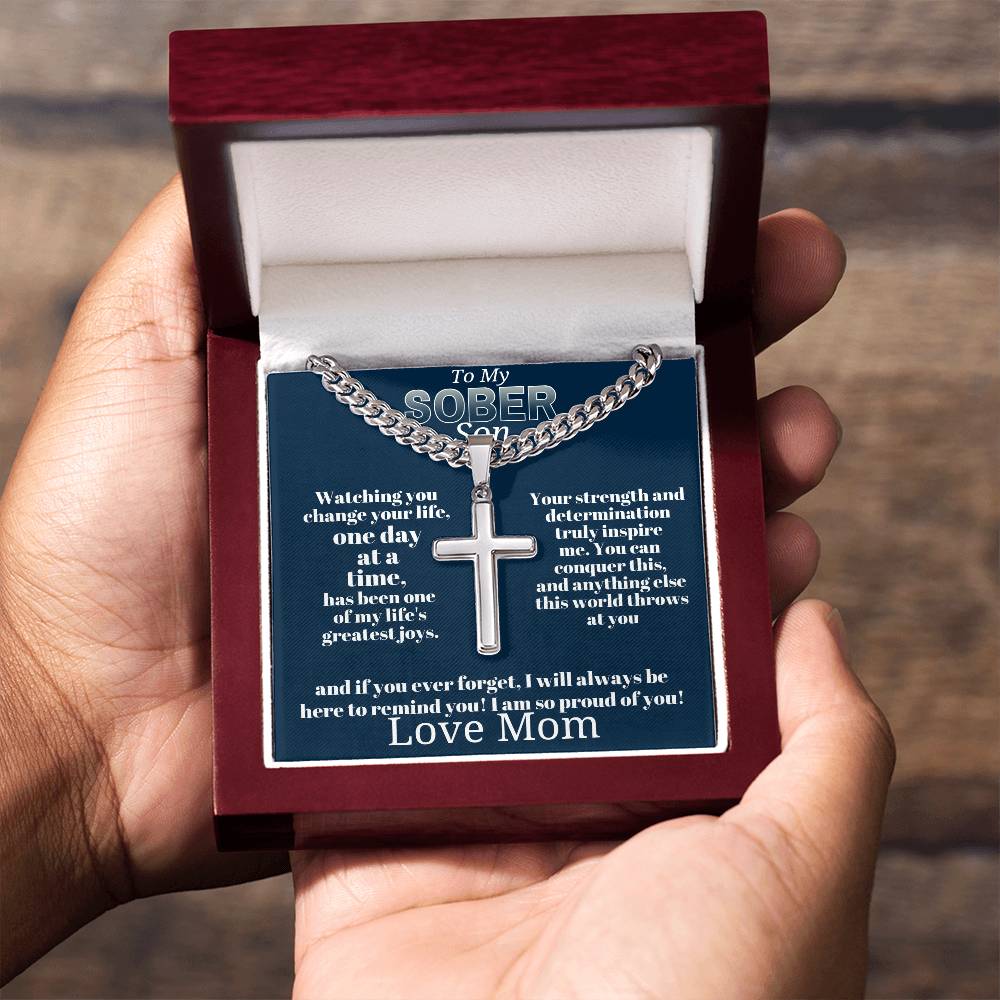 Silver-tone cross pendant necklace in open wooden gift box held in hands