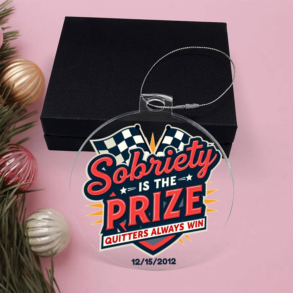 Round hanging ornament in front of black gift box with ribbon loop and “Sobriety Is The Prize”
