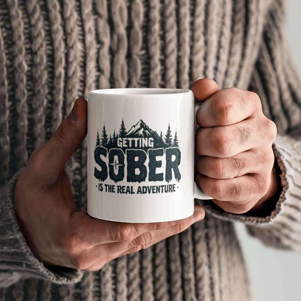 Hands holding a white ceramic mug with black 'GETTING SOBER' slogan