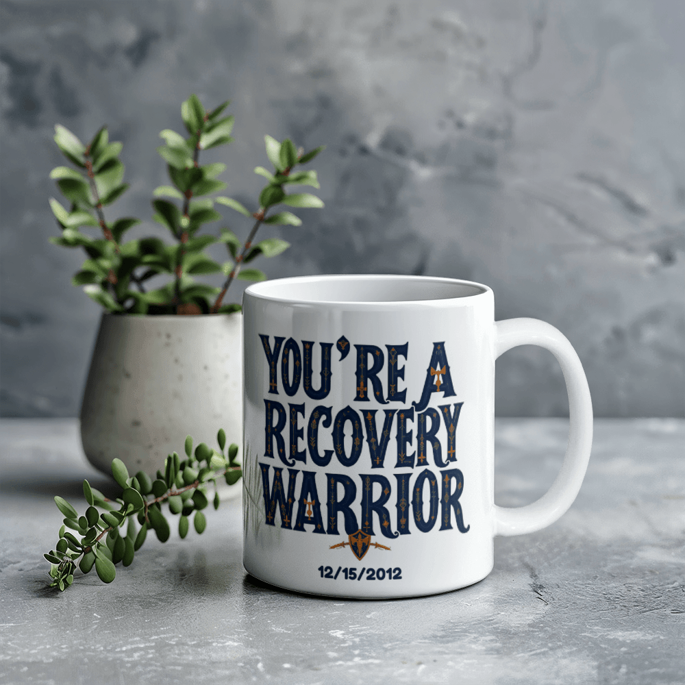 White coffee mug on tabletop with “You’re a Recovery Warrior” print and date