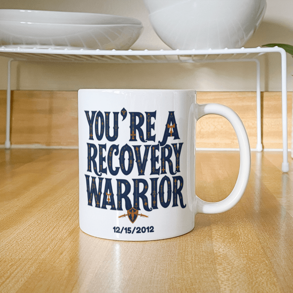 White coffee mug showing “You’re a Recovery Warrior” graphic with handle and date