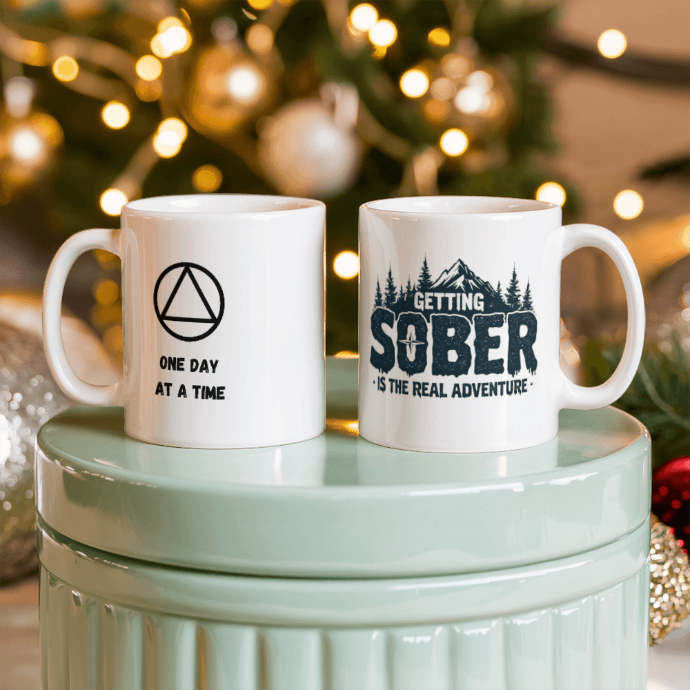 Two white ceramic mugs: 'ONE DAY AT A TIME' and 'GETTING SOBER' with pine trees