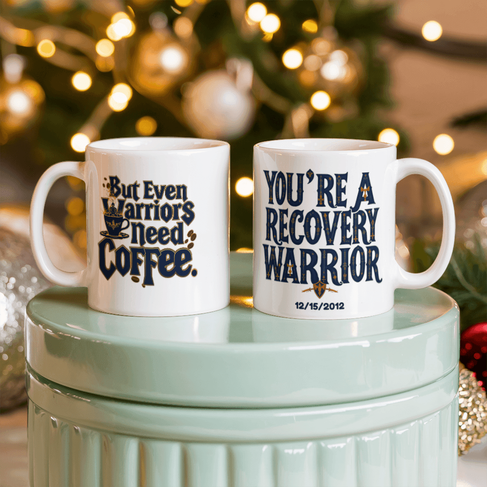 Two white coffee mugs on a stand; one reads “You’re a Recovery Warrior” with date