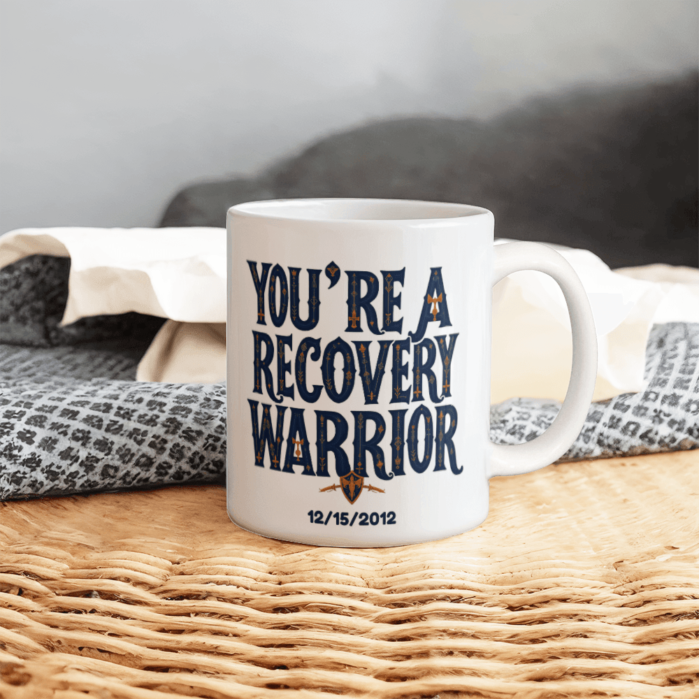 White ceramic coffee mug with “You’re a Recovery Warrior” text and emblem, date print