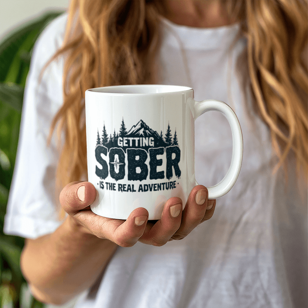 Hands holding a white ceramic mug with black 'GETTING SOBER' slogan