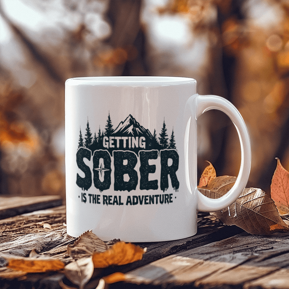 White ceramic mug on a surface with black 'GETTING SOBER' and 'is the real adventure'