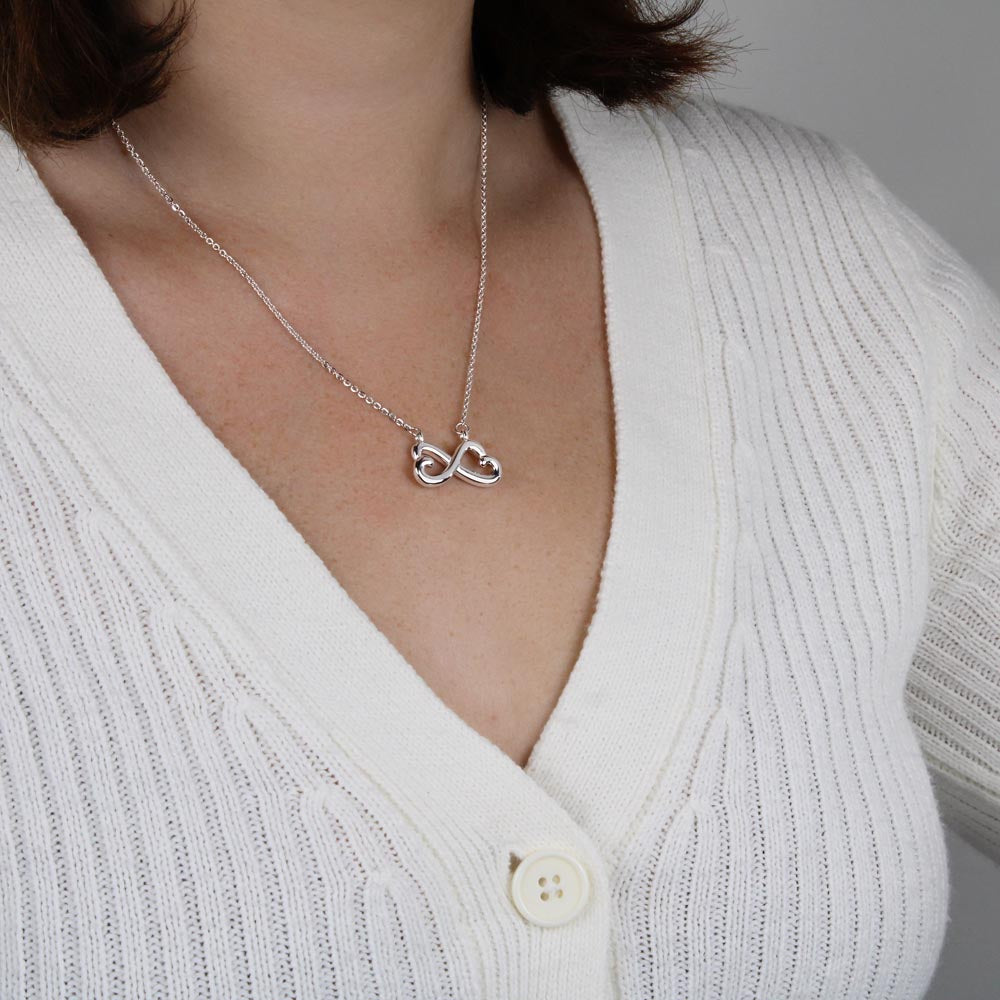 Silver infinity necklace with heart charm on a V-neck knit sweater