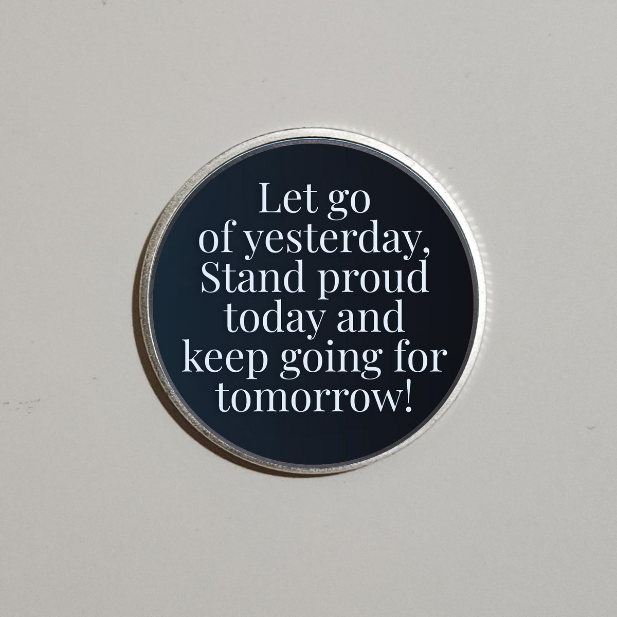 Silver-rimmed round recovery coin with dark blue quote panel, “Let go of yesterday”.
