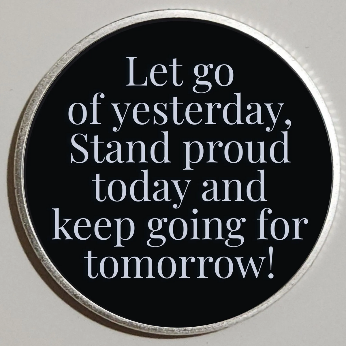 Round coin with black face and quote: Let go of yesterday; stand proud today and keep going tomorrow!