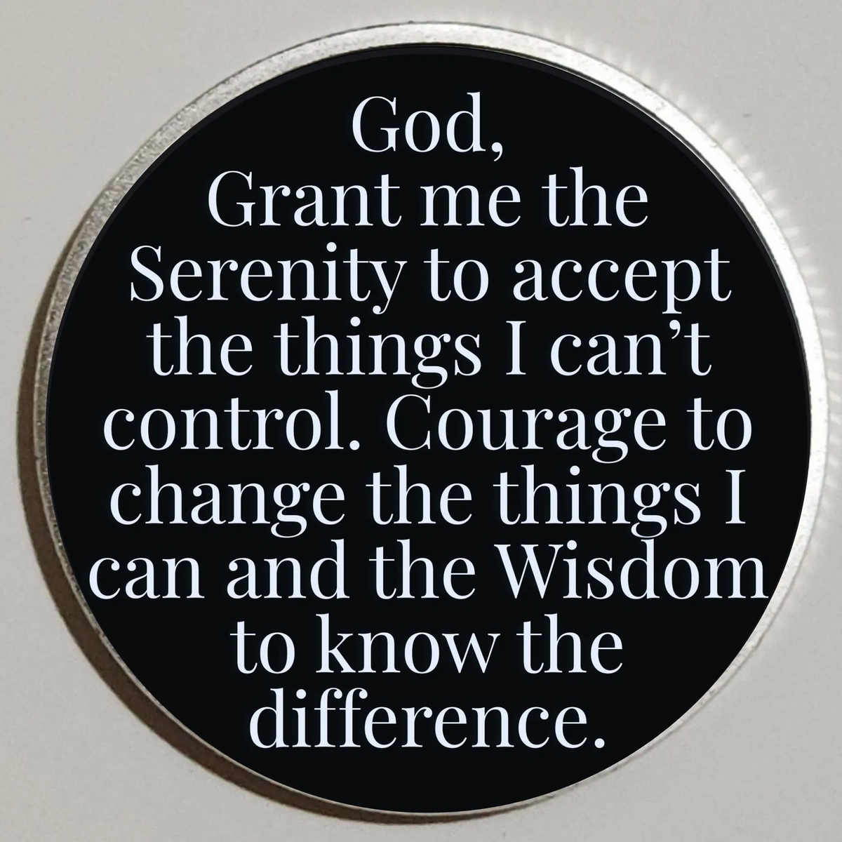 Round coin with black face and quote text: God, grant me the serenity to accept what I can’t control.