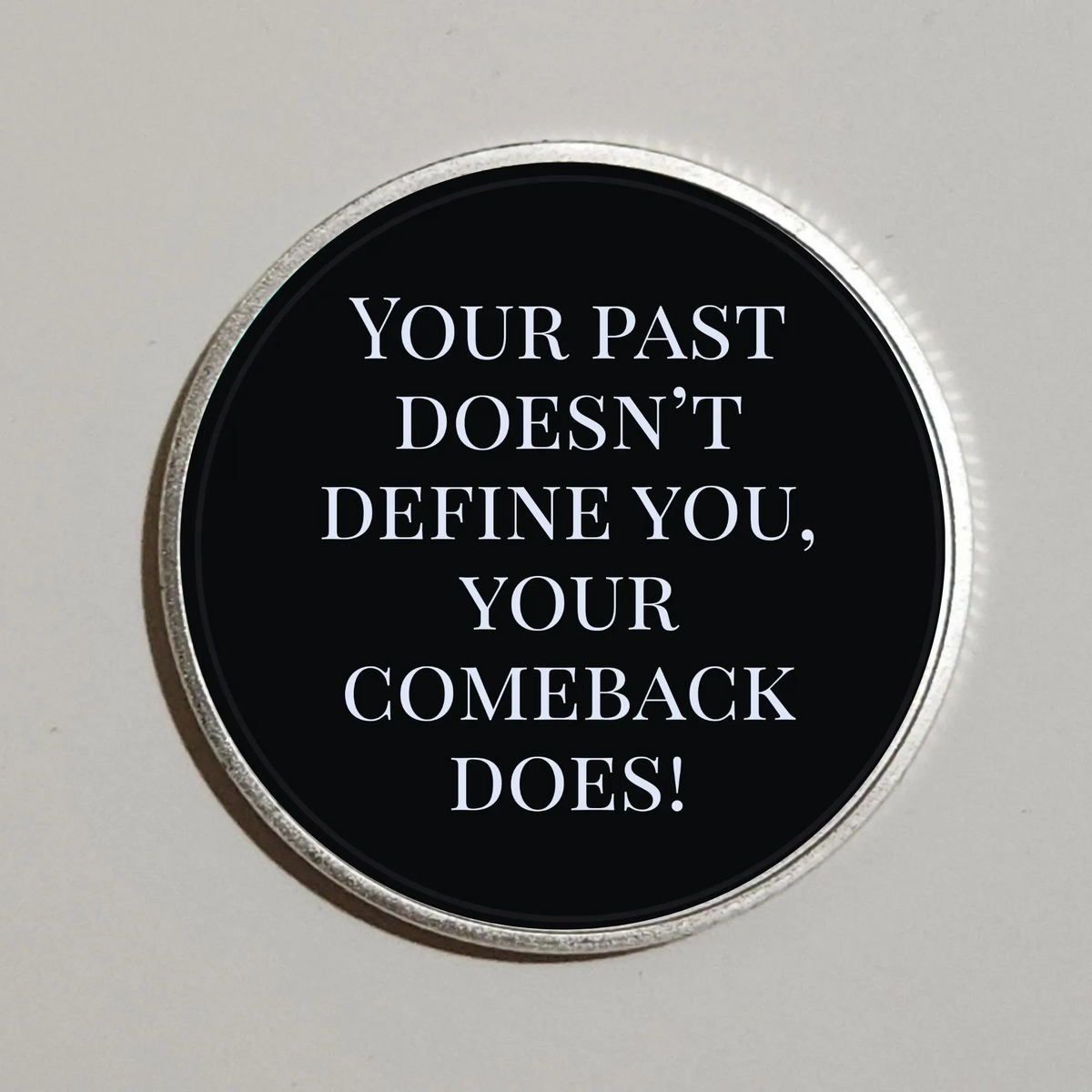 Round coin with black face and quote: Your past doesn't define you; your comeback does!
